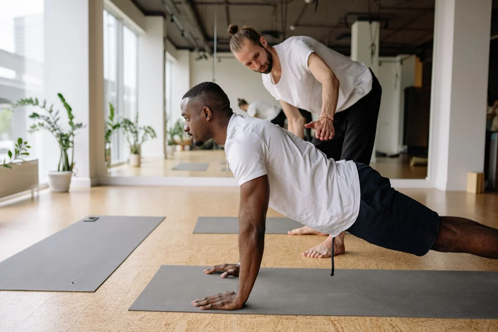 A yoga teacher guiding a student through a stretch